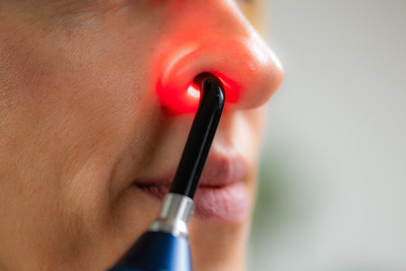 Woman undergoing red light therapy for nasal treatment, using a specialized device to relieve sinus congestion, improve breathing, and reduce inflammation in a clinical or home setting.の写真素材