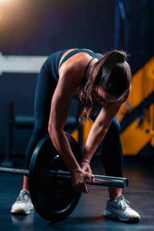 Weight placement on a barbell involves a woman, readying for training to enhance strength in a supportive gym environment.の写真素材