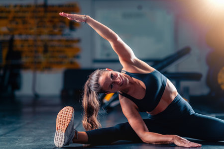Stretching after training in the gym, a woman improves flexibility and reduces muscle tension. This...