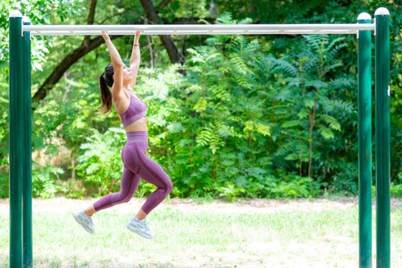 Female athlete performing monkey bar endurance drills outdoors, focusing on muscle strength,...