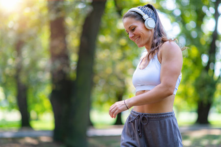 Active woman enjoying outdoor walk in sportswear and headphones, maintaining rhythm, breathing, and focus. Promotes balance and healthy recreation.の写真素材
