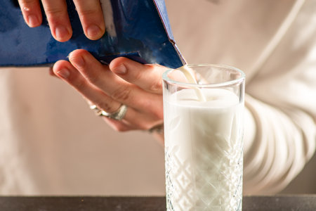 Person preparing milk in a glass cup. Focus on foam texture, aroma, and elegant presentationの写真素材
