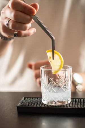 Professional barman preparing gin cocktail, adding fresh lemon slice into glass. Highlights aroma, freshness, and elegant mixology style.の写真素材