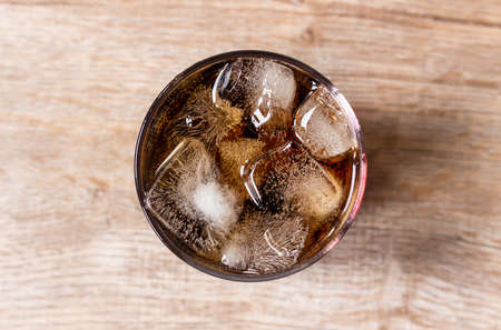 Top view of cola and ice in clear glass on wooden tableの写真素材