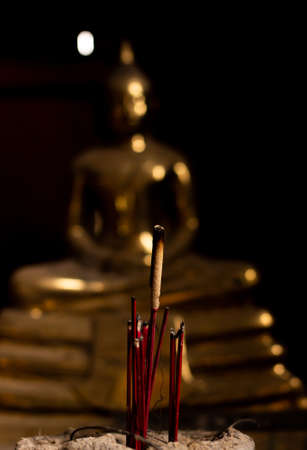 Close up incense in front of the golden buddha and black backgroundの写真素材