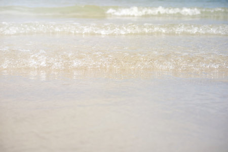 Clear water of waves on sandy beach and light of sun