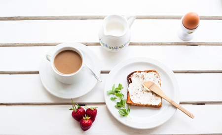 Table set for a typical breakfast with poached eggs, coffee, milk and toastの写真素材
