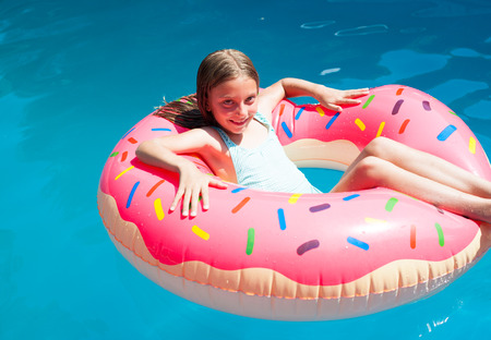 Happy little girl laying on a colorful inflatable donut  in a  swimming pool.