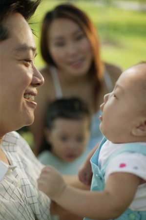 Father carrying baby, mother and young daughter in the background.の写真素材
