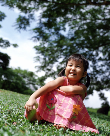 Girl sitting on grass, tree in backgroundの写真素材
