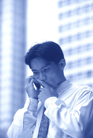 Male executive using cellular phone, thoughtful expressionの写真素材