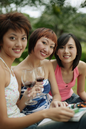 Young women sitting, looking at camera, wine glasses in handの写真素材