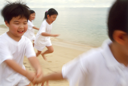 Children in white outfits running along the beachの写真素材