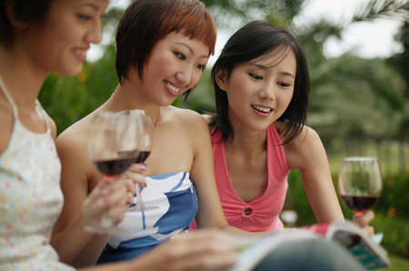 Young women browsing through magazine, wine glasses in handの写真素材