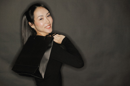 Young woman carrying shopping bag, black backgroundの写真素材