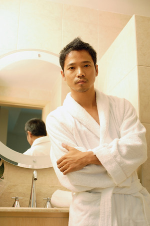 Young man in robe with arms crossed, looking at cameraの写真素材