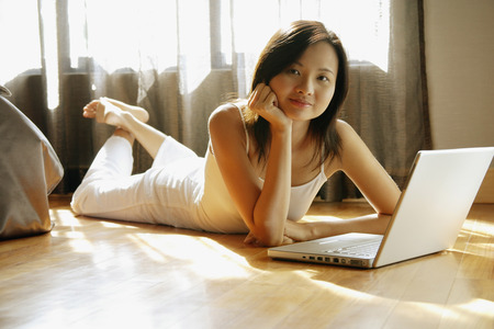 Young woman lying on floor, hand on chin, looking at cameraの写真素材