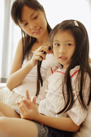 Mother and daughter, sitting side by side, daughter looking at cameraの写真素材