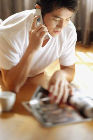 Young man reading magazine while on the phoneの写真素材