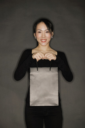 Young woman carrying shopping bag, black backgroundの写真素材