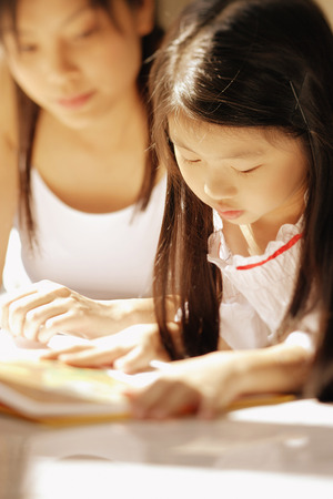 Mother and daughter, side by side, looking at magazineの写真素材