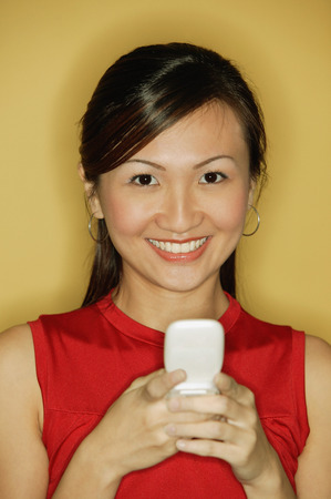 Young woman wearing a red top, holding a mobile phoneの写真素材