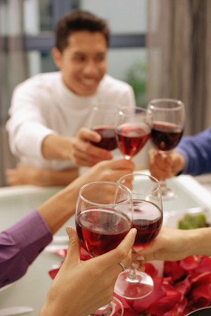 Friends toasting with wine glasses across dinner tableの写真素材