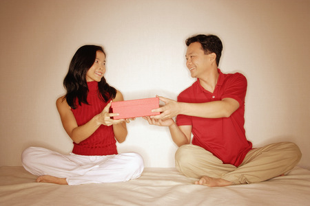 Man and woman sitting side by side, legs crossed, holding a box between them.の写真素材