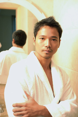 Young man in robe with arms crossed, looking at cameraの写真素材