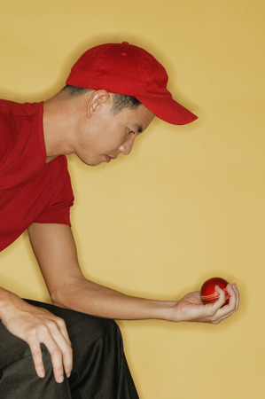 Young man sitting down and holding a ball in his handの写真素材