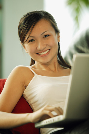 Young woman on sofa, using laptop, looking at cameraの写真素材