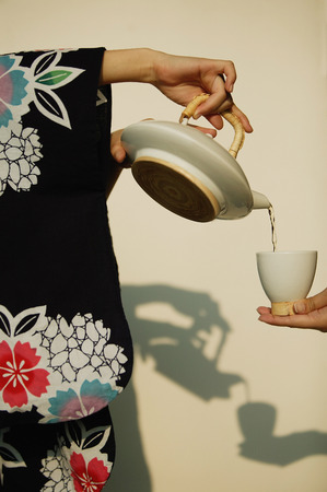 Young woman in kimono pouring tea for someone.の写真素材
