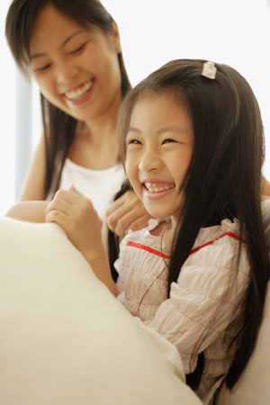 Mother and daughter, sitting side by side, laughing while mother braids daughter's hair.の写真素材