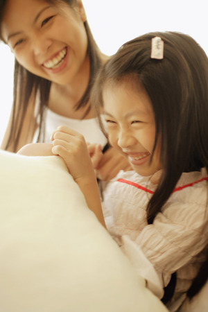 Mother and daughter, sitting side by side, laughingの写真素材