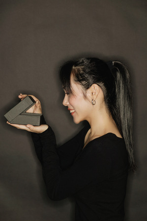 Young woman, side view, opening a box, black backgroundの写真素材