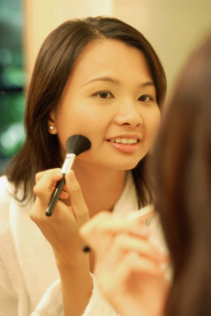 Woman putting on make-up with a blush brushの写真素材