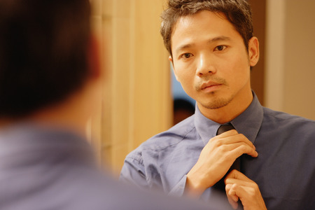 Young man adjusting tie, looking in mirrorの写真素材
