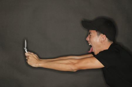 Young man holding mobile phone, making a faceの写真素材