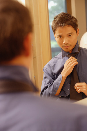 Young man  looking in mirror, adjusting tieの写真素材