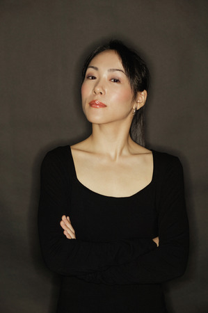Young woman, arms crossed, standing against a black backgroundの写真素材