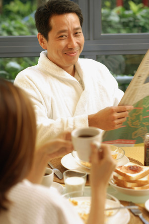 Couple at breakfast table, man holding newspaperの写真素材
