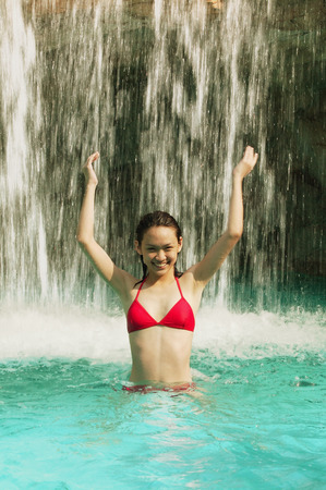 Young woman in swimming pool, water cascading on herの写真素材