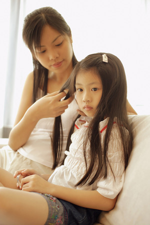 Mother and daughter, sitting side by side, mother braiding daughter's hair.の写真素材