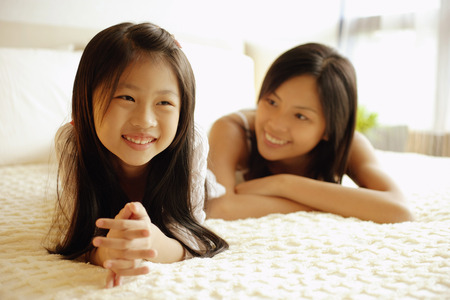 Mother and daughter lying on bed, smilingの写真素材