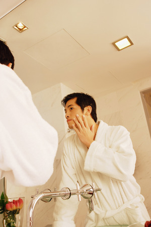 Young man touching his face, looking in mirrorの写真素材
