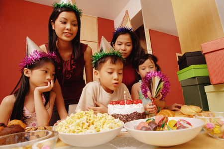 Young boy blowing out candles on a cake, surrounded by friendsの写真素材