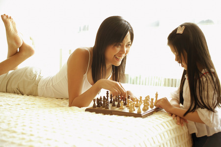 Mother and daughter playing chess in bedroomの写真素材