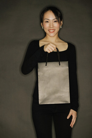 Young woman carrying shopping bag, black backgroundの写真素材