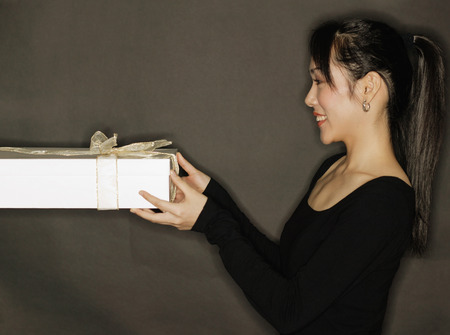 Young woman holding a gift, black backgroundの写真素材