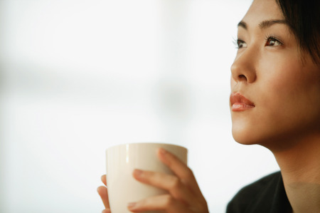 Young woman sitting at desk, holding mugの写真素材